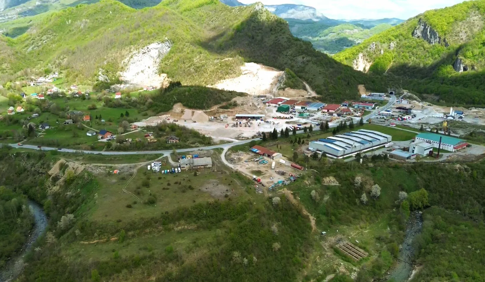 Pogled iz vazduha na industrijsku zonu okruženu brdima i zelenilom.