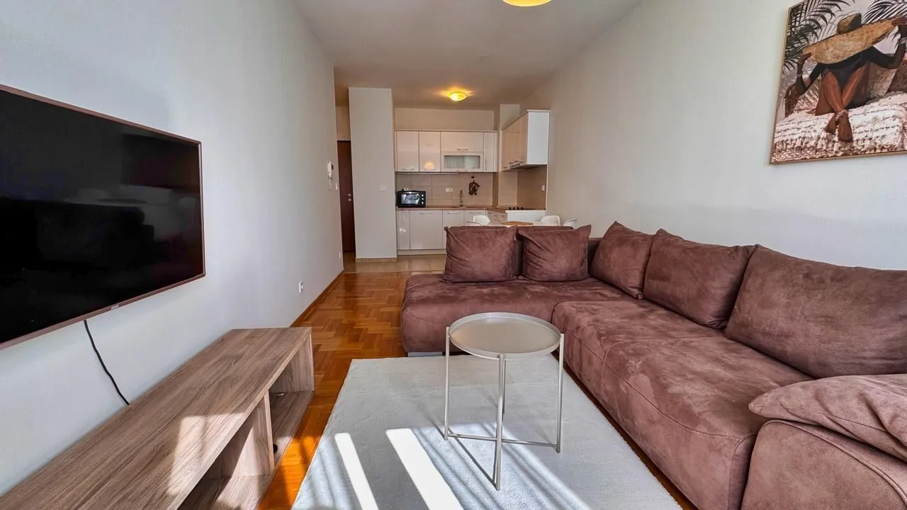 Living room with a corner sofa, television, and a view of the kitchen in the background.