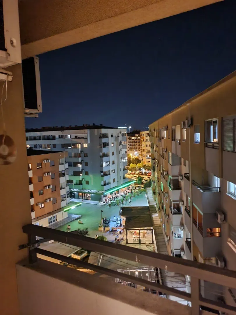 Night view from a balcony showing surrounding buildings and a paved courtyard.