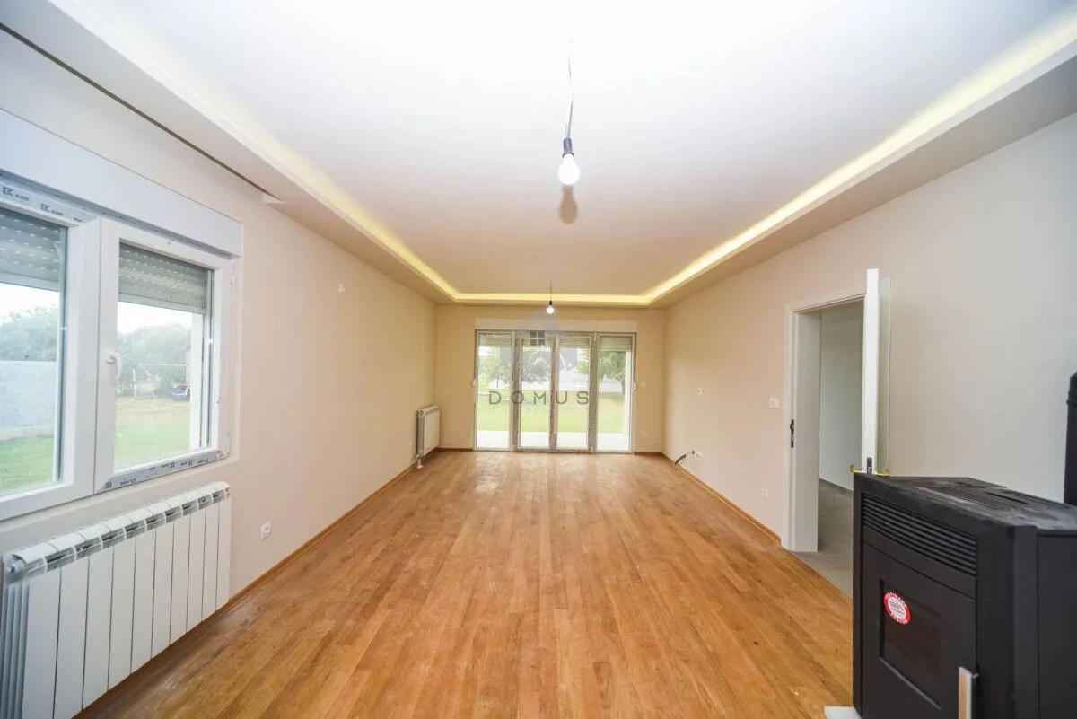 Empty living room with wooden flooring, pellet stove, and a view of the yard.