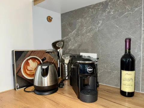 Detalj kuhinje sa aparatom za kafu, kuvalom i flašom vina na radnoj površini. - image 11