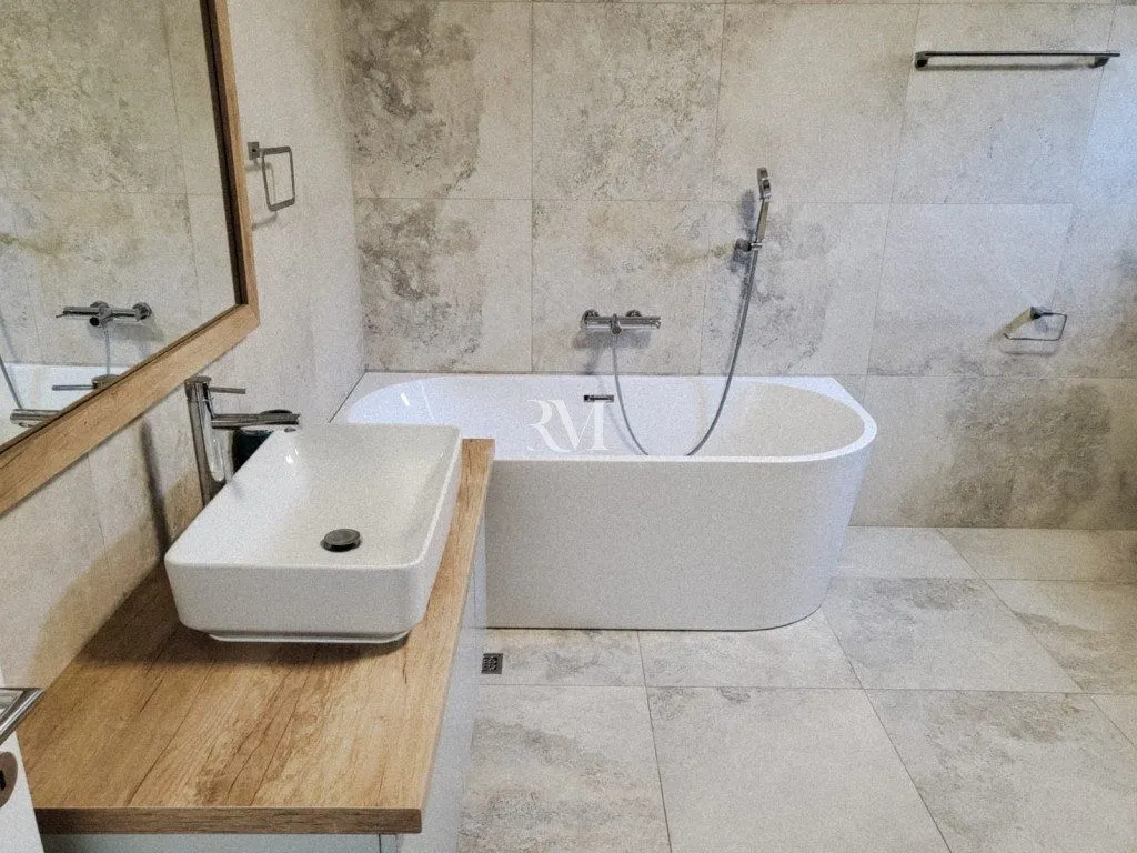 Modern bathroom equipped with a bathtub, washbasin, and neutral-toned tiles.