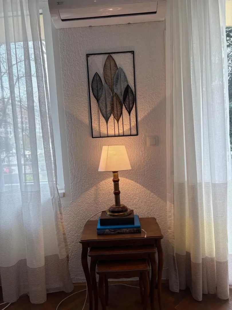 A corner of a room featuring a decorative lamp, nesting tables, and curtains.