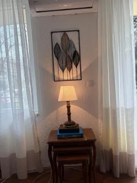 A corner of a room featuring a decorative lamp, nesting tables, and curtains. - image 7