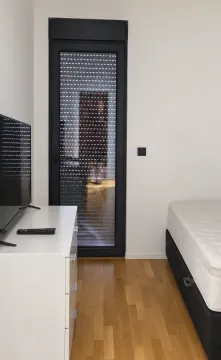 Spavaća soba sa krevetom, komodom, televizorom i balkonskim vratima. - image 8