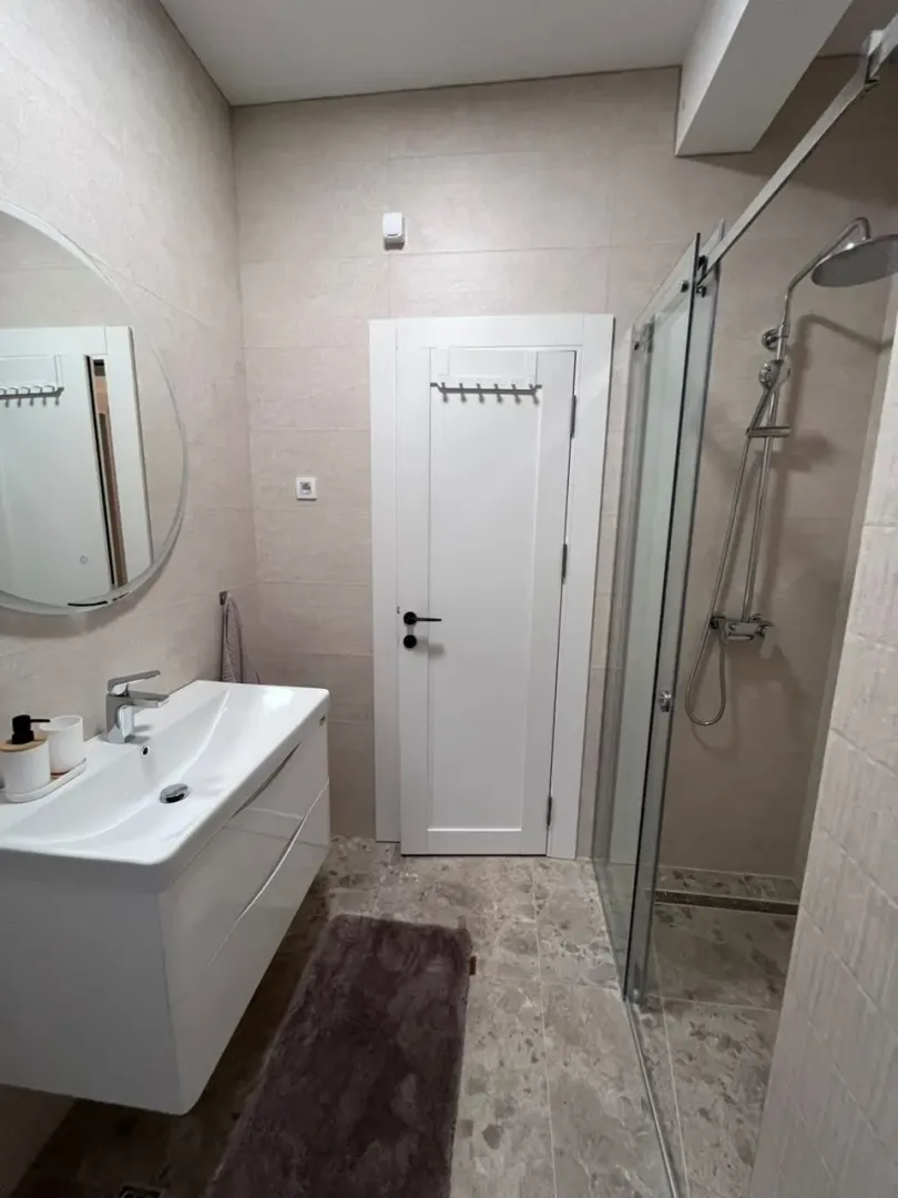 Modern bathroom with a sink, glass shower cabin, and a mirror.