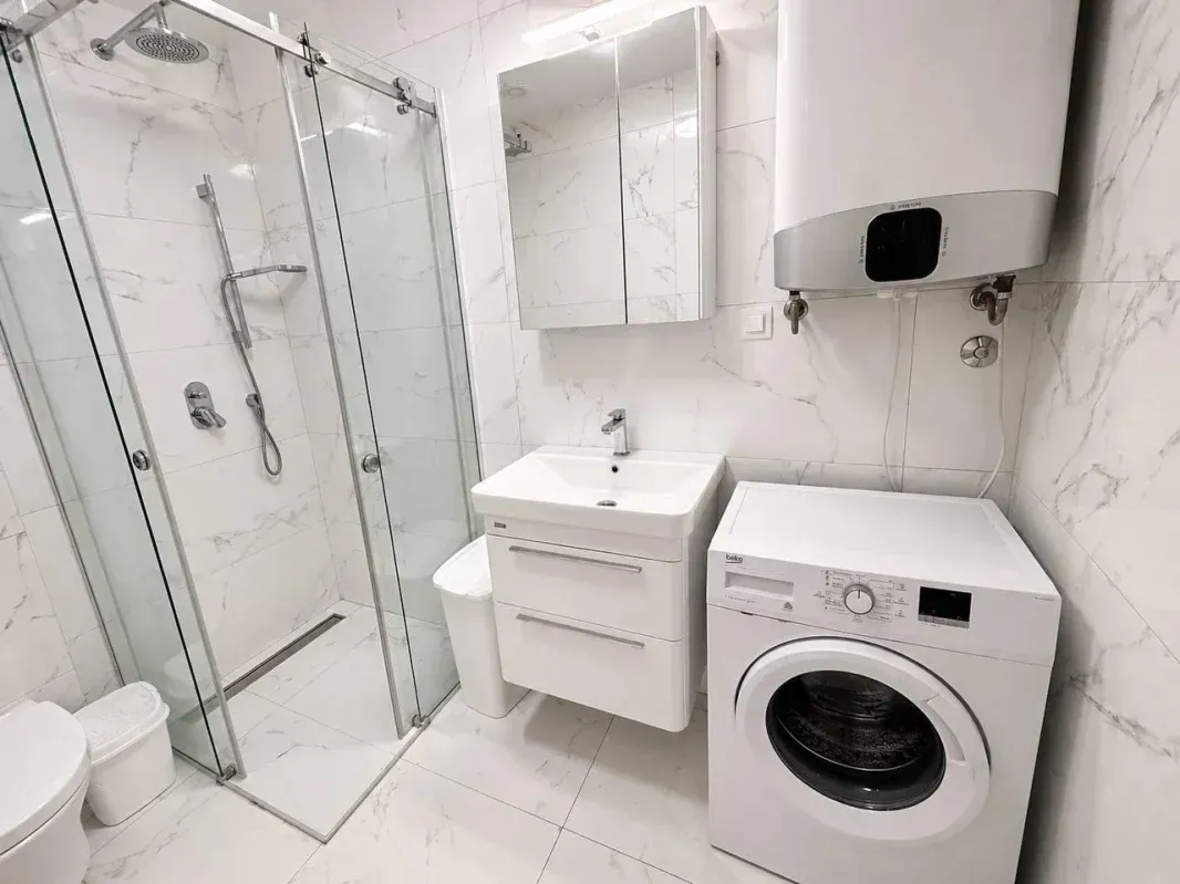 Modern bathroom with a shower cabin, sink, and washing machine.
