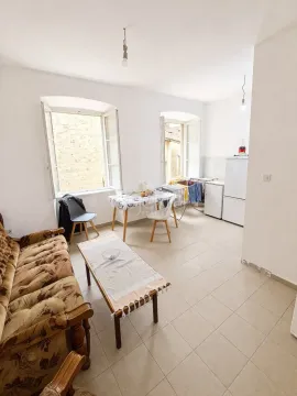 Living room with a sofa, dining table, and kitchen area in the background. - image 6
