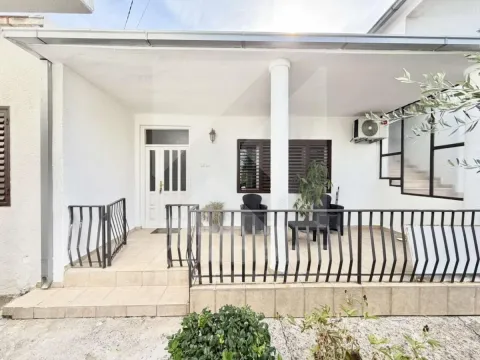 Covered terrace in front of the house entrance with a railing and seating set. - image 11