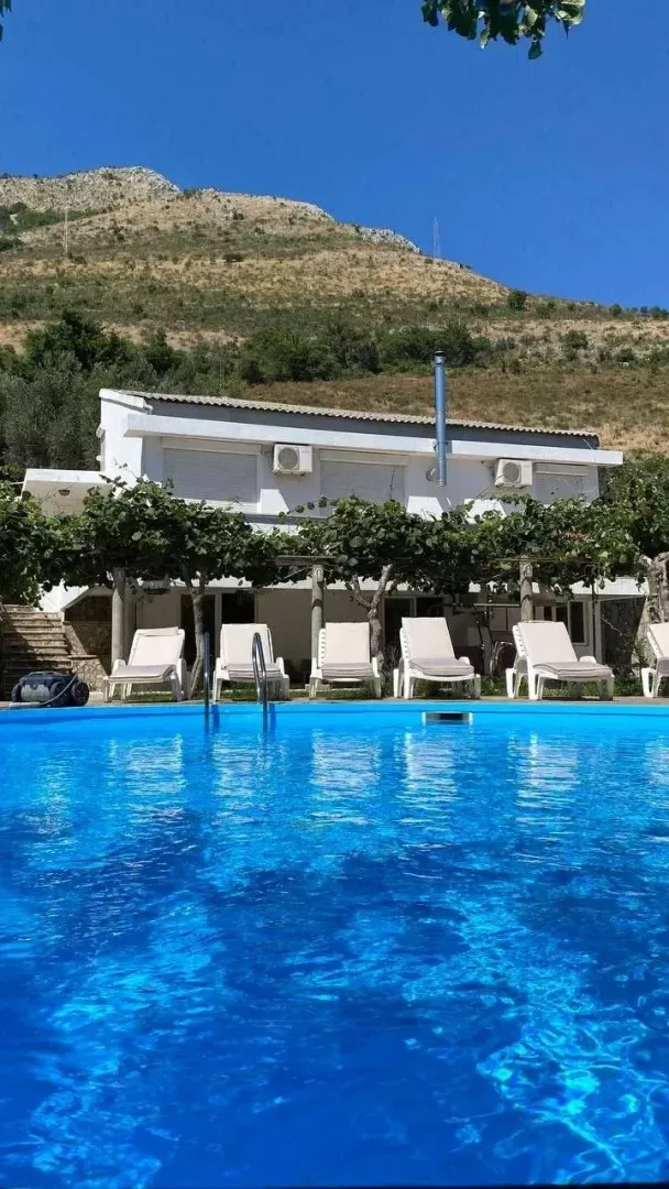 Eksterijer kuće sa bazenom, ležaljkama i pogledom na brdo.