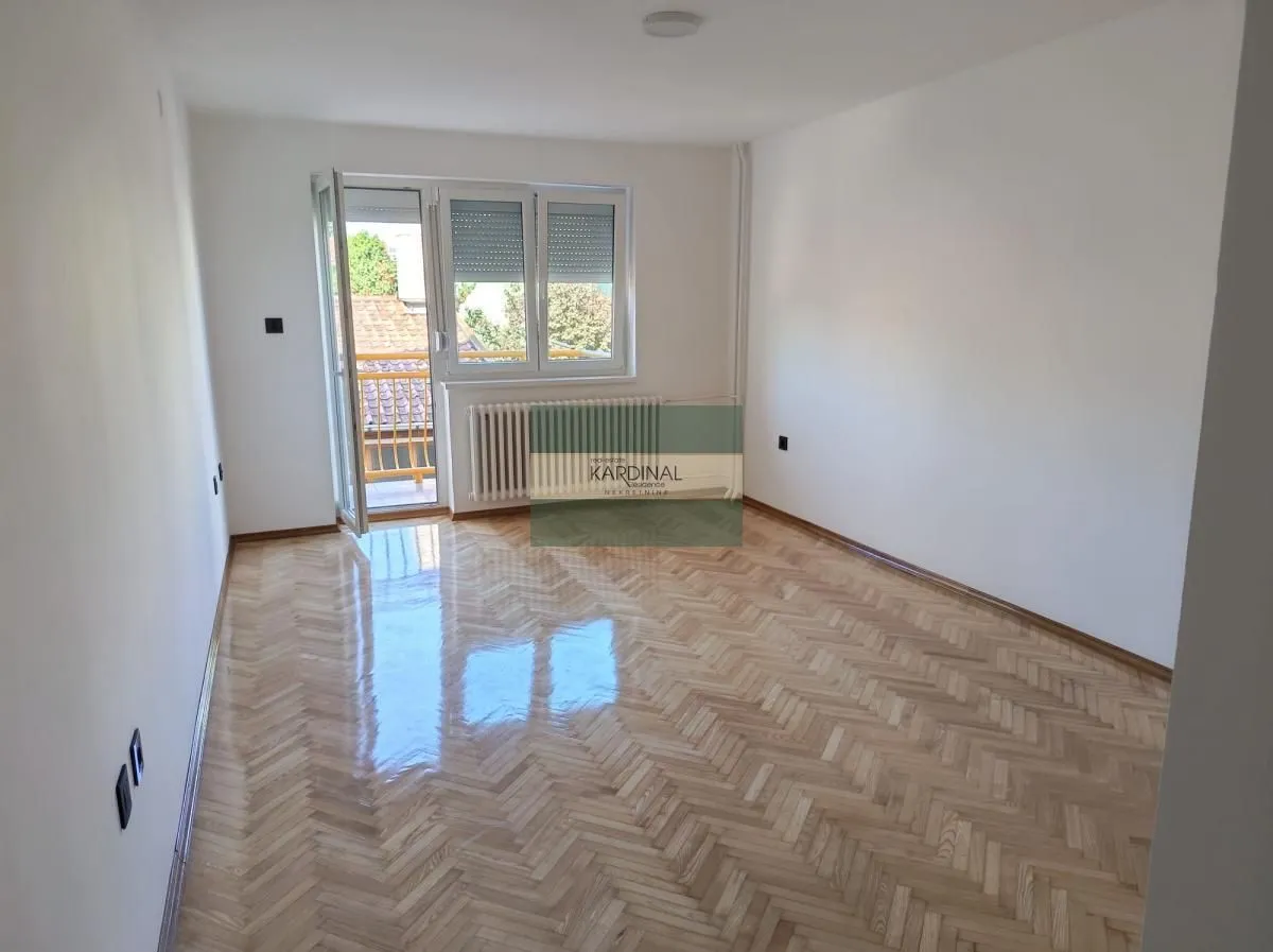 Prazna neopremljena soba sa parketom i izlazom na balkon.