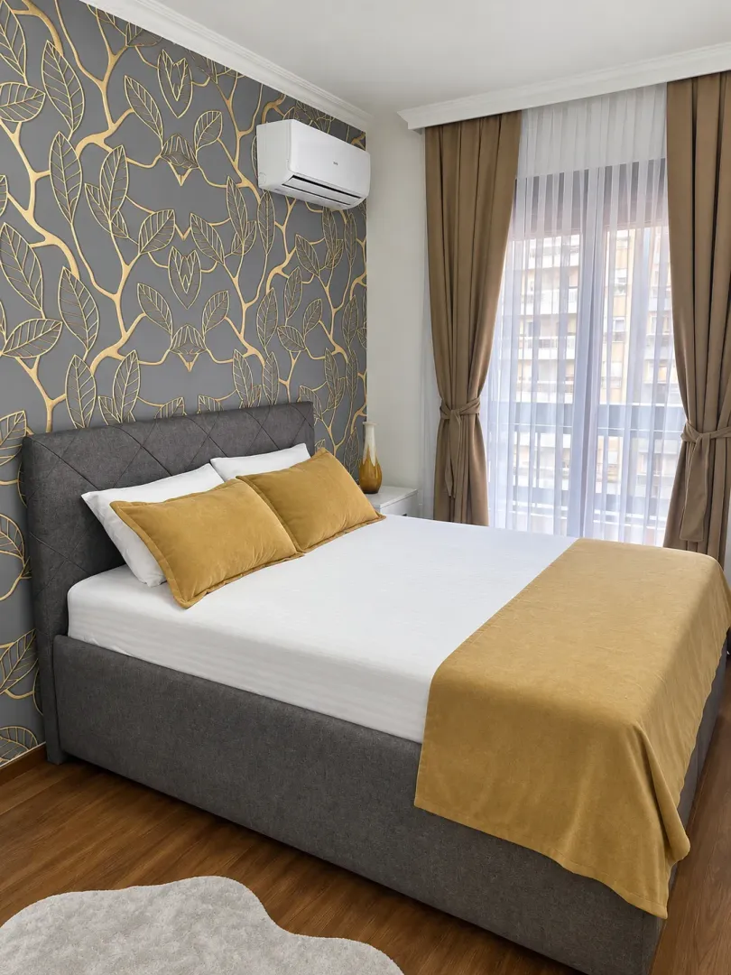 Furnished bedroom with a double bed, patterned wallpaper, and an air conditioner.
