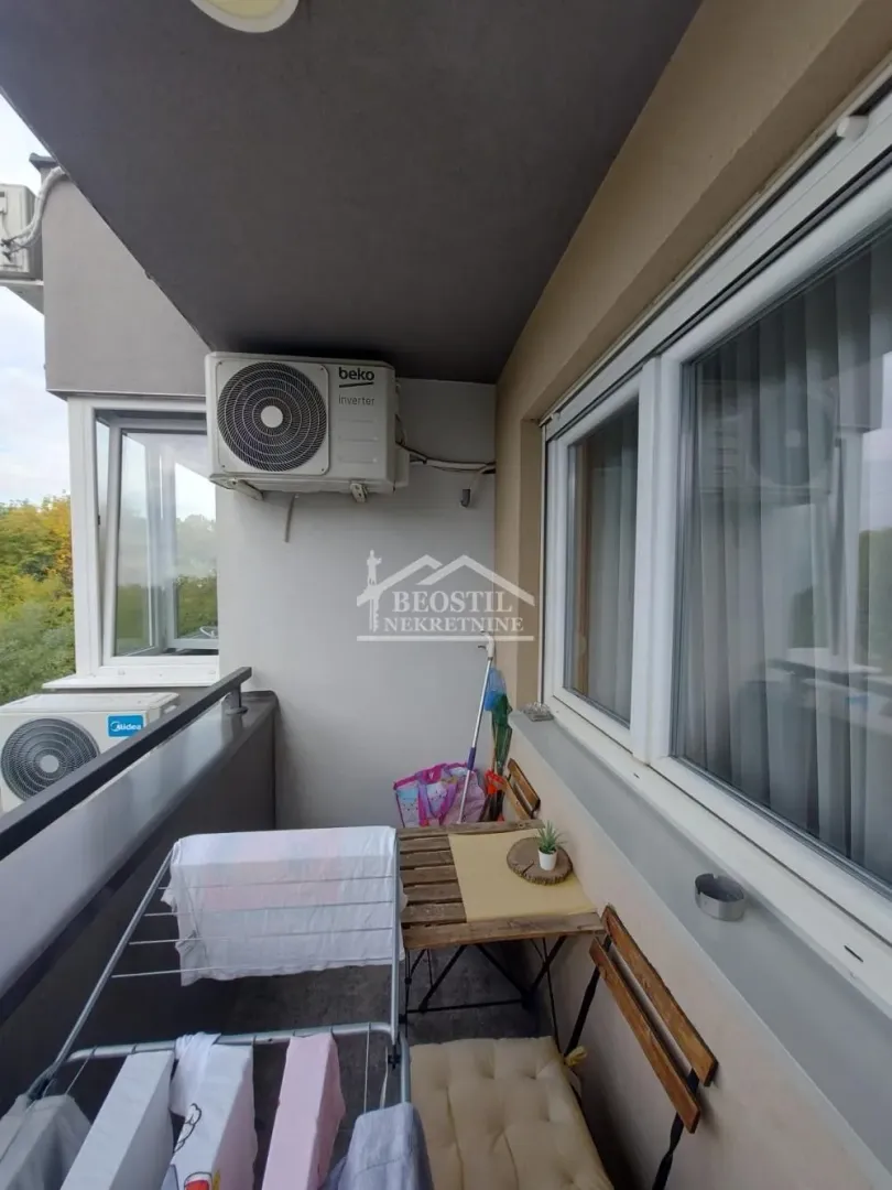Manji balkon sa klima uređajem, stolom i stalkom za sušenje veša.