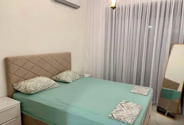 Furnished bedroom with a double bed, white curtains, and a mirror.
