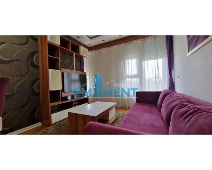 Living room with a purple sofa, wooden TV unit, and a window with curtains.