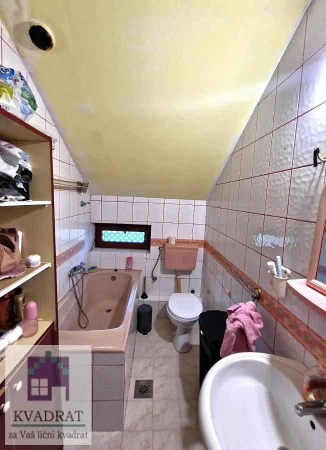 Smaller bathroom with a bathtub, toilet, and washbasin under a sloped ceiling.