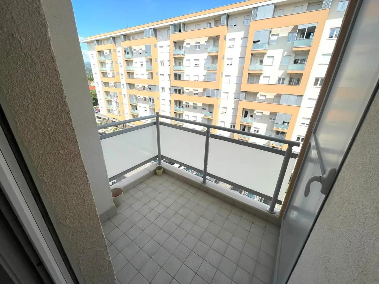 Manji popločani balkon sa ogradom i pogledom na susjednu zgradu.