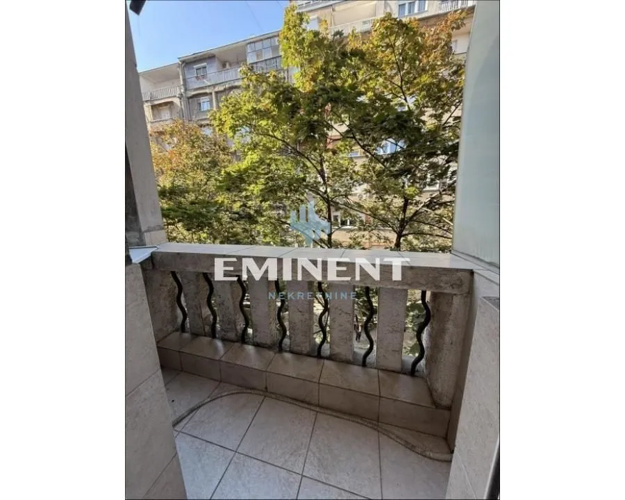 Manji popločani balkon sa kamenom ogradom i pogledom na drveće.