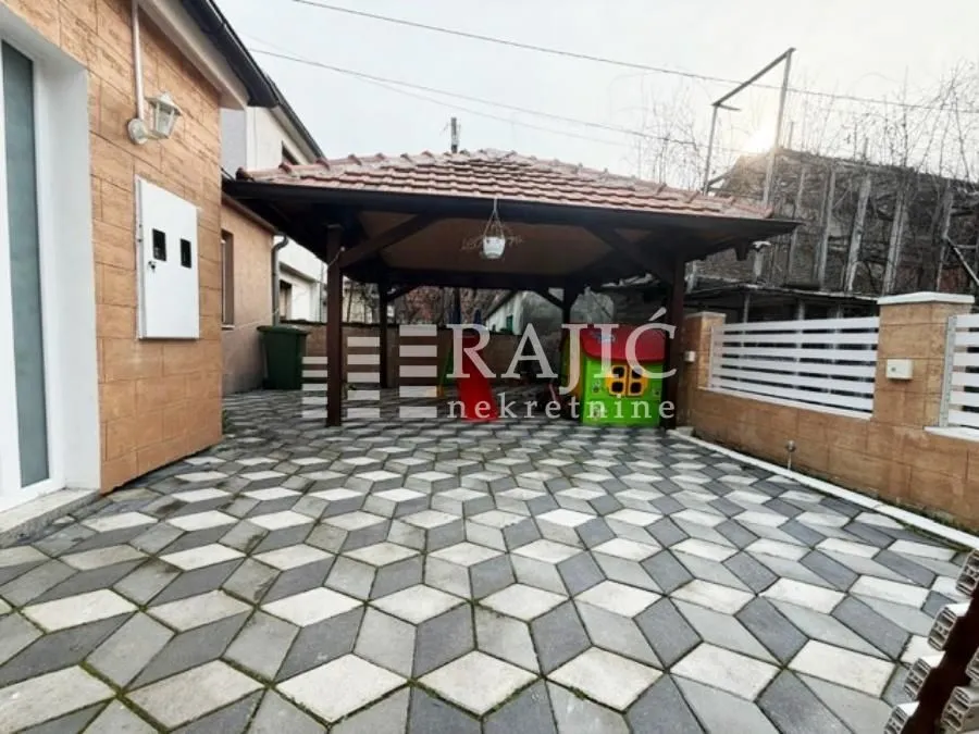 Dvorište kuće sa popločanim podom i natkrivenom drvenom nadstrešnicom.