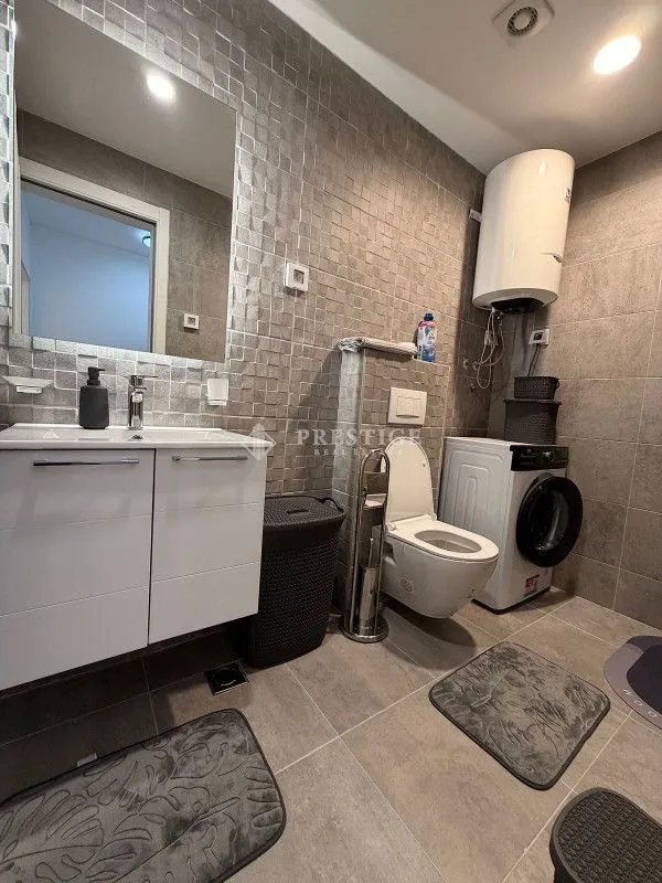 Modernly equipped bathroom with a shower, sink, and washing machine.