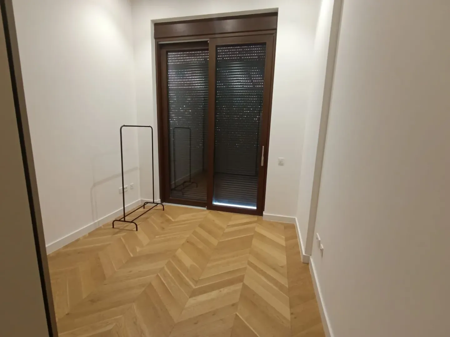 Prazna prostorija sa parketom i balkonskim vratima.