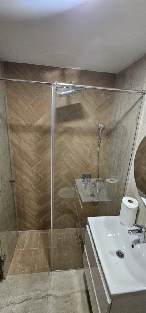 Moderno kupatilo sa staklenom tuš kabinom i lavaboom.