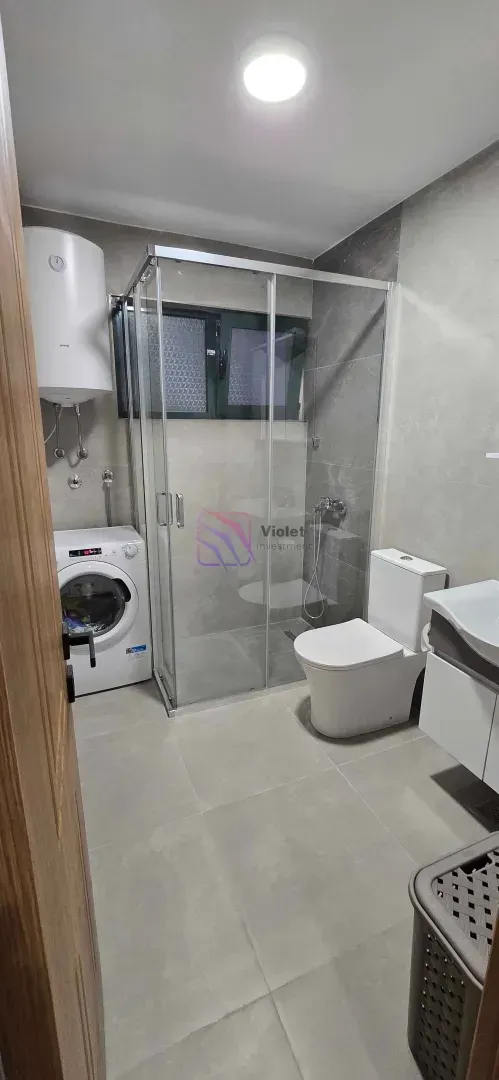 Moderne kupatilo sa tuš kabinom, umivaonikom, WC šoljom i mašinom za veš.