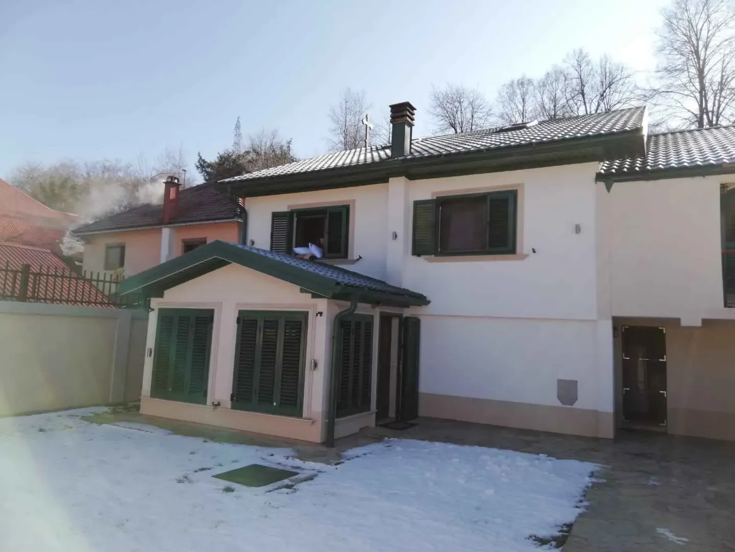 Pogled na dvorište i fasadu kuće sa snijegom.