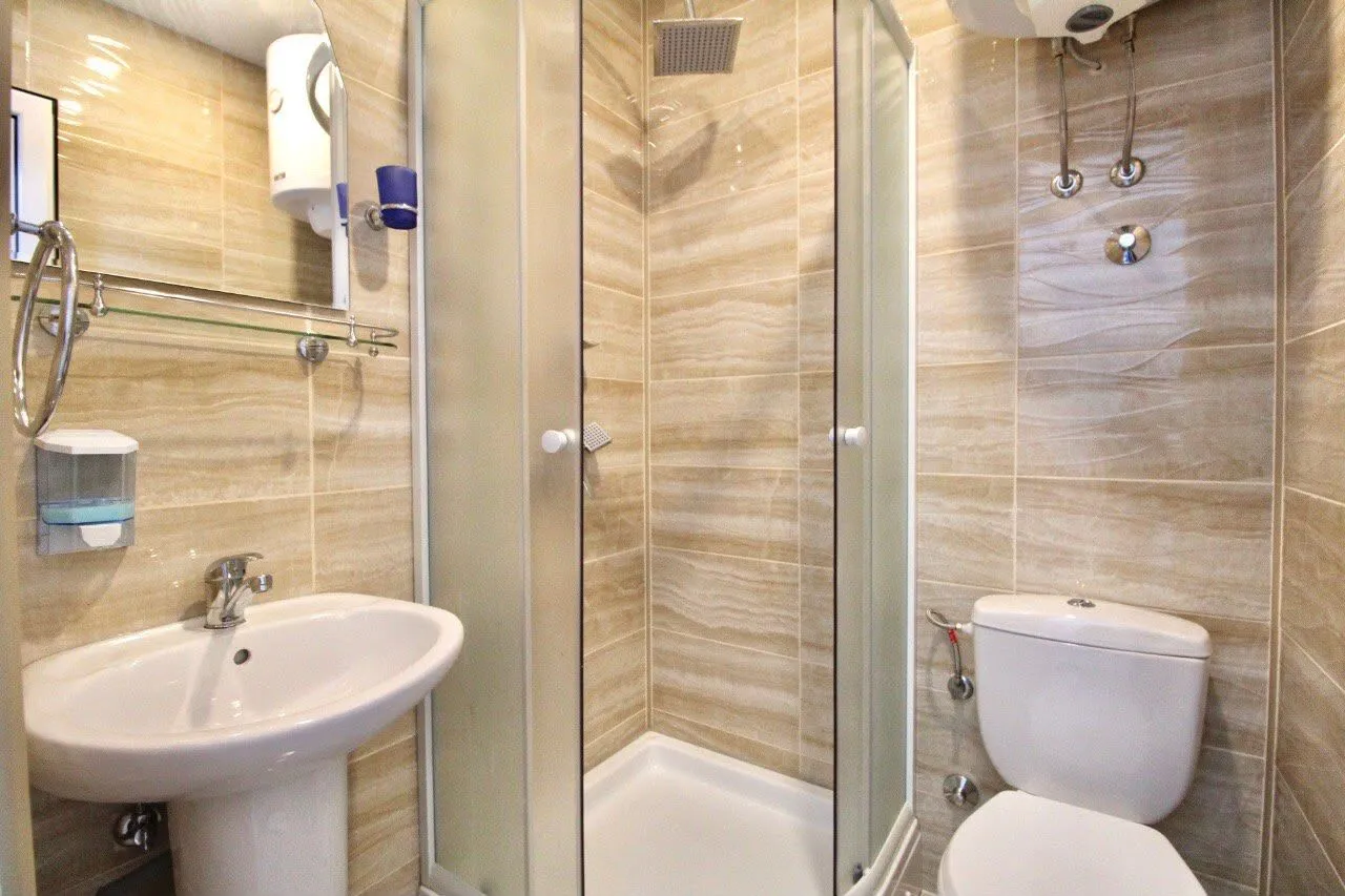 Compact bathroom with a shower cabin, sink, and toilet in beige tiles.