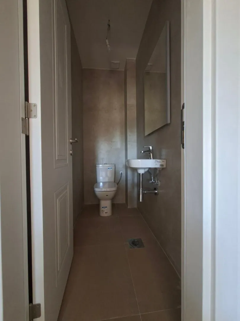 Pogled na moderno opremljeno kupatilo sa wc šoljom, umivaonikom i ogledalom.