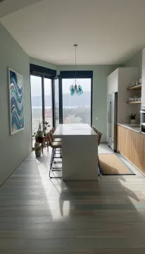 Moderna kuhinja sa šankom i trpezarijskim stolom, svijetlim drvenim detaljima i pogledom na more. - image 13