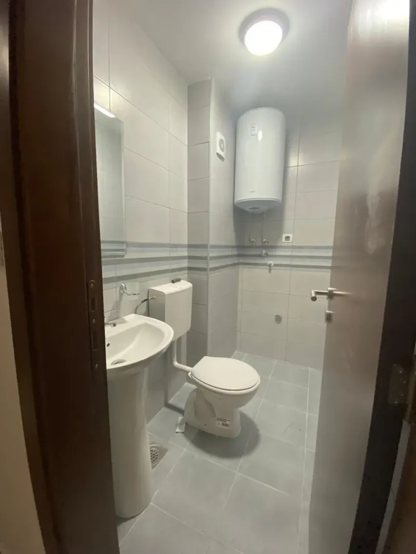 Manje kupatilo sa svijetlim pločicama, umivaonikom i wc šoljom.