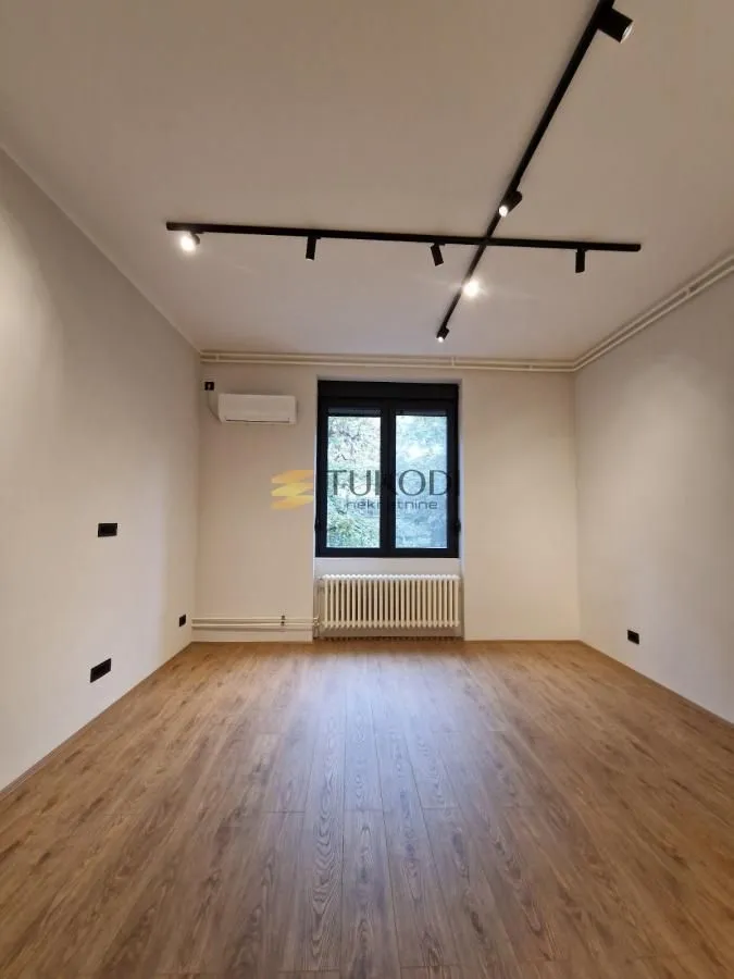 Empty room with laminate flooring, white walls, and black ceiling lighting.