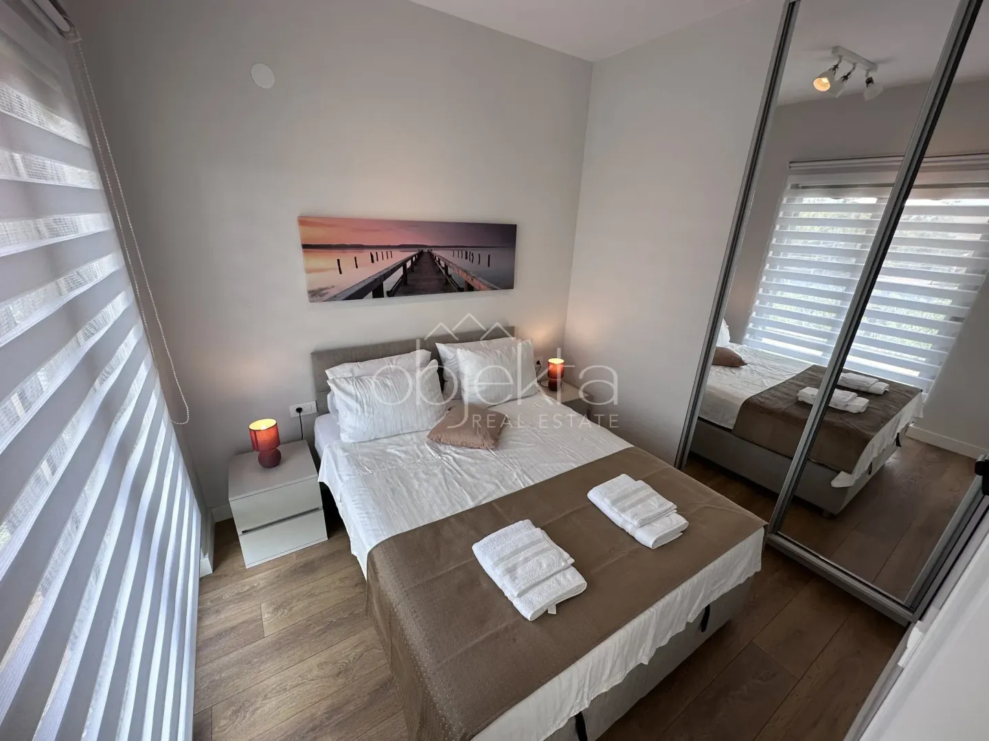 Furnished bedroom with a double bed, bedside tables, and a large mirrored built-in wardrobe.