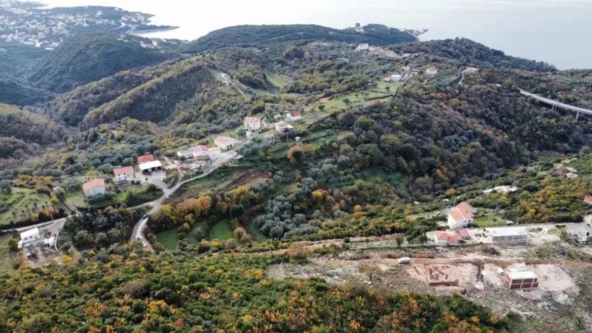 Pogled iz vazduha na brdoviti pejzaž sa selom i okolnim rastinjem.