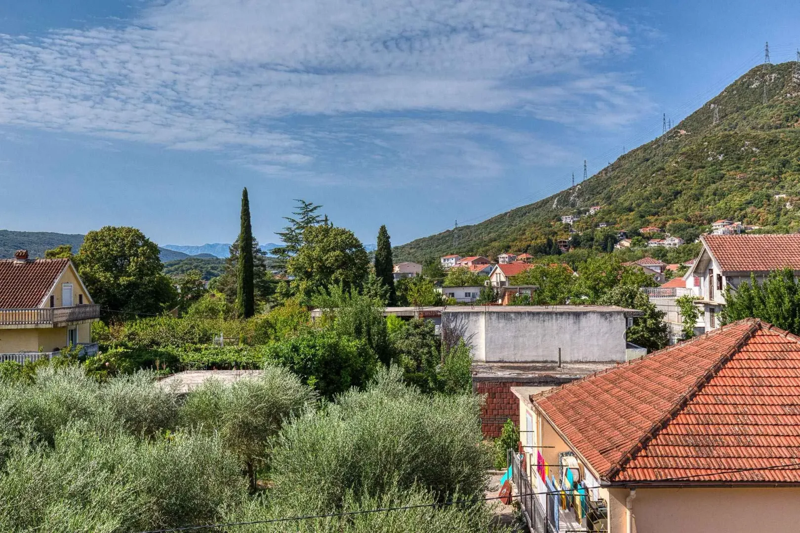 Pogled na okolno zelenilo, kuće i brda iz daljine.