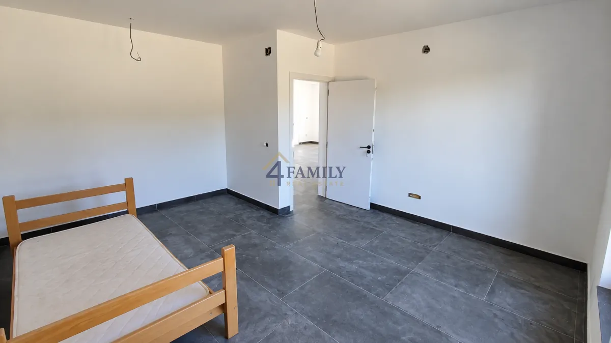 Empty room with grey floor tiles and a wooden bed.