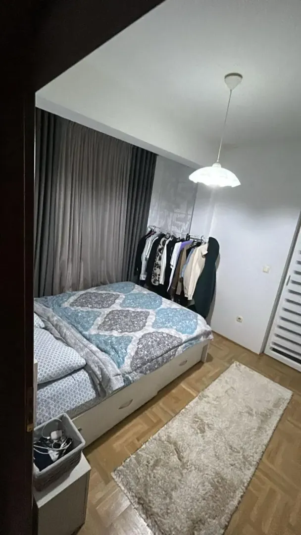 Namještena spavaća soba sa bračnim krevetom, garderoberom i parketom na podu.