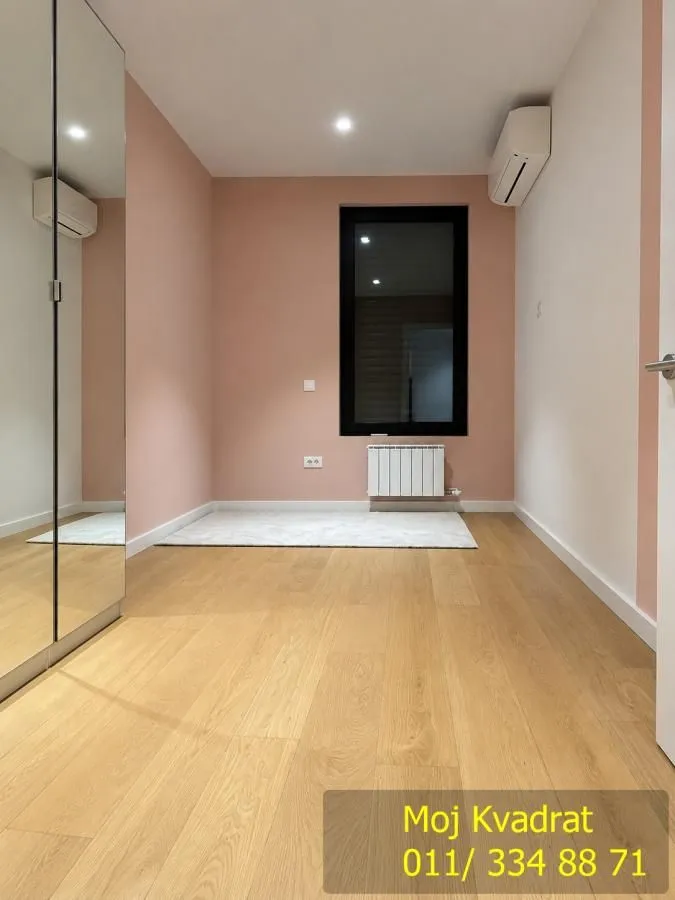 Empty bedroom with a pink accent wall, wooden flooring, and a mirrored built-in wardrobe.