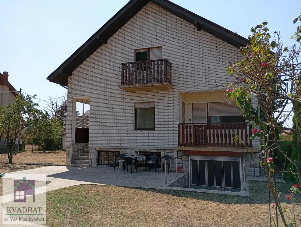 Pogled na zadnju stranu kuće sa fasadom od cigle, balkonima i popločanim dvorištem.