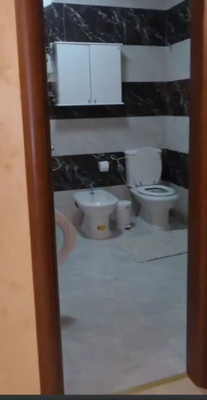 Pogled na kupatilo sa sanitarijama i crno-bijelim pločicama kroz vrata.