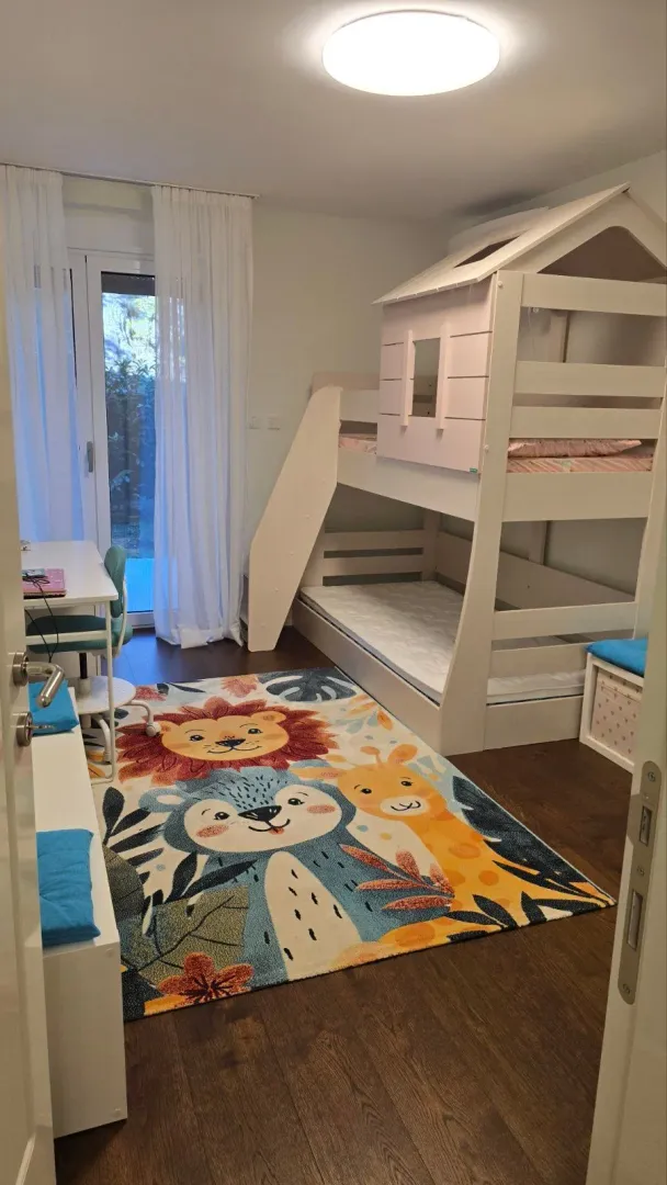 Children's bedroom with a bunk bed, desk, and colorful rug.