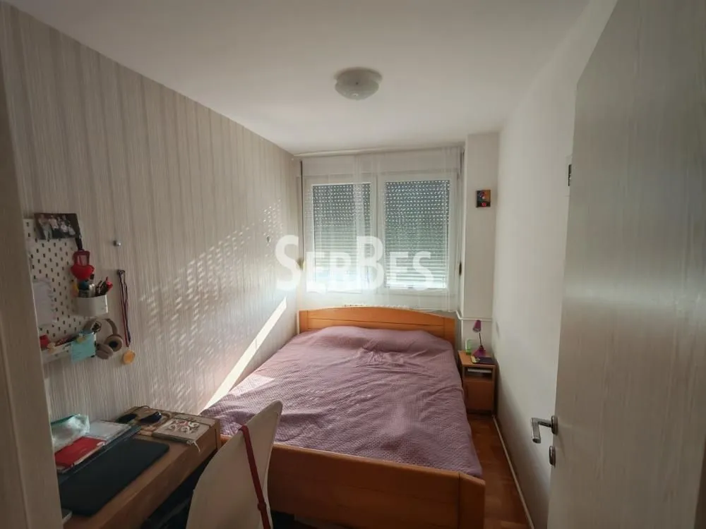 Manja spavaća soba sa bračnim krevetom i radnim stolom.