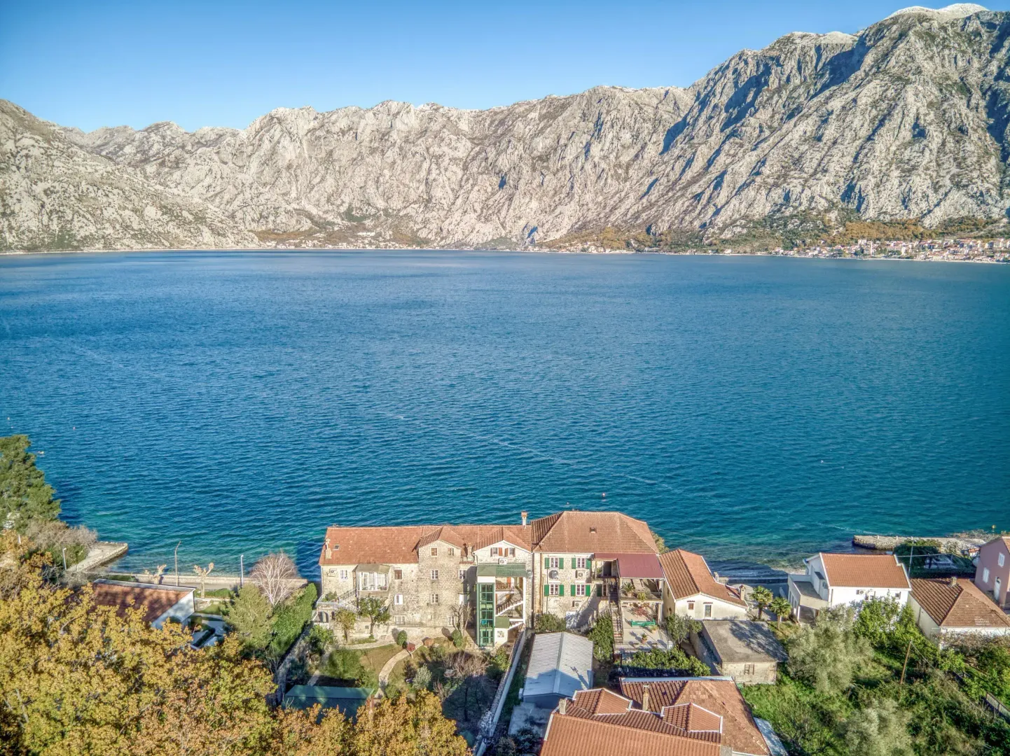 Aerial view of a stone house by the sea with mountains in the background.