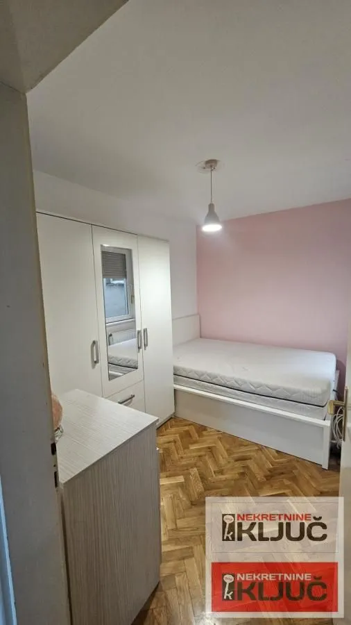 Manja spavaća soba sa krevetom, garderoberom i parketom na podu.