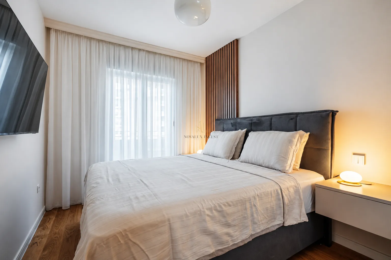 Modern bedroom with a double bed, wall-mounted TV, and bedside table.
