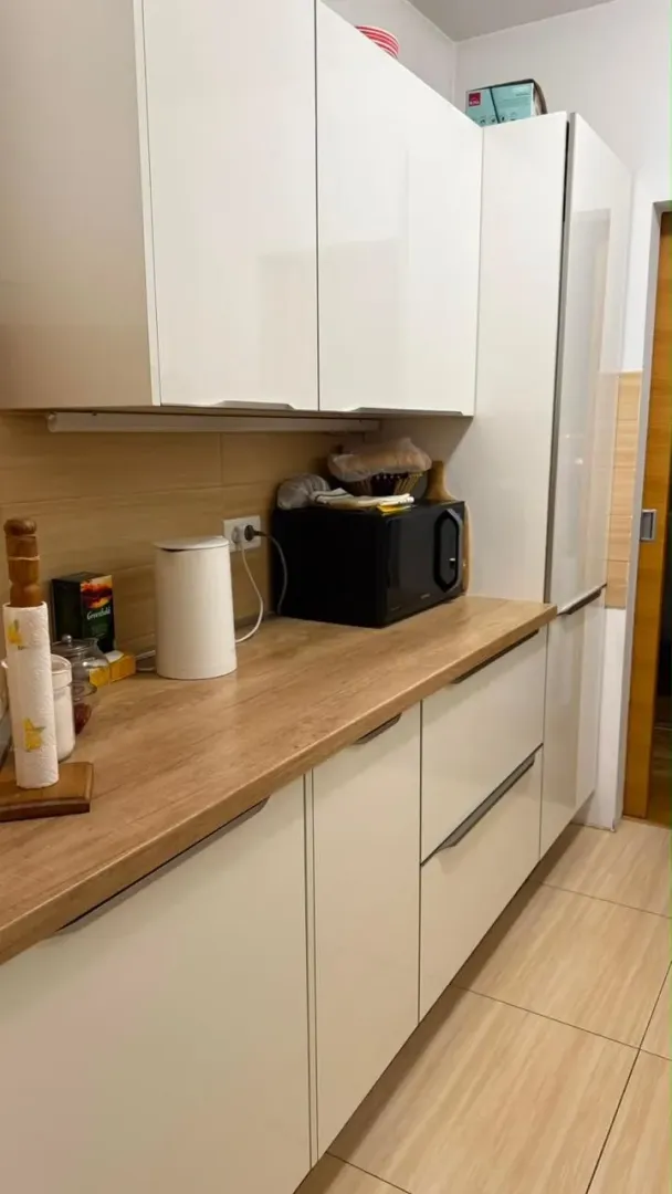 Moderna kuhinja sa bijelimelementima i drvenom radnom pločom.