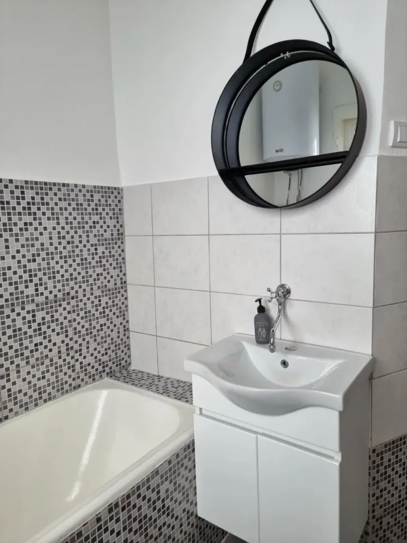 Bathroom with a sink, mirror, and bathtub tiled with mosaic tiles.