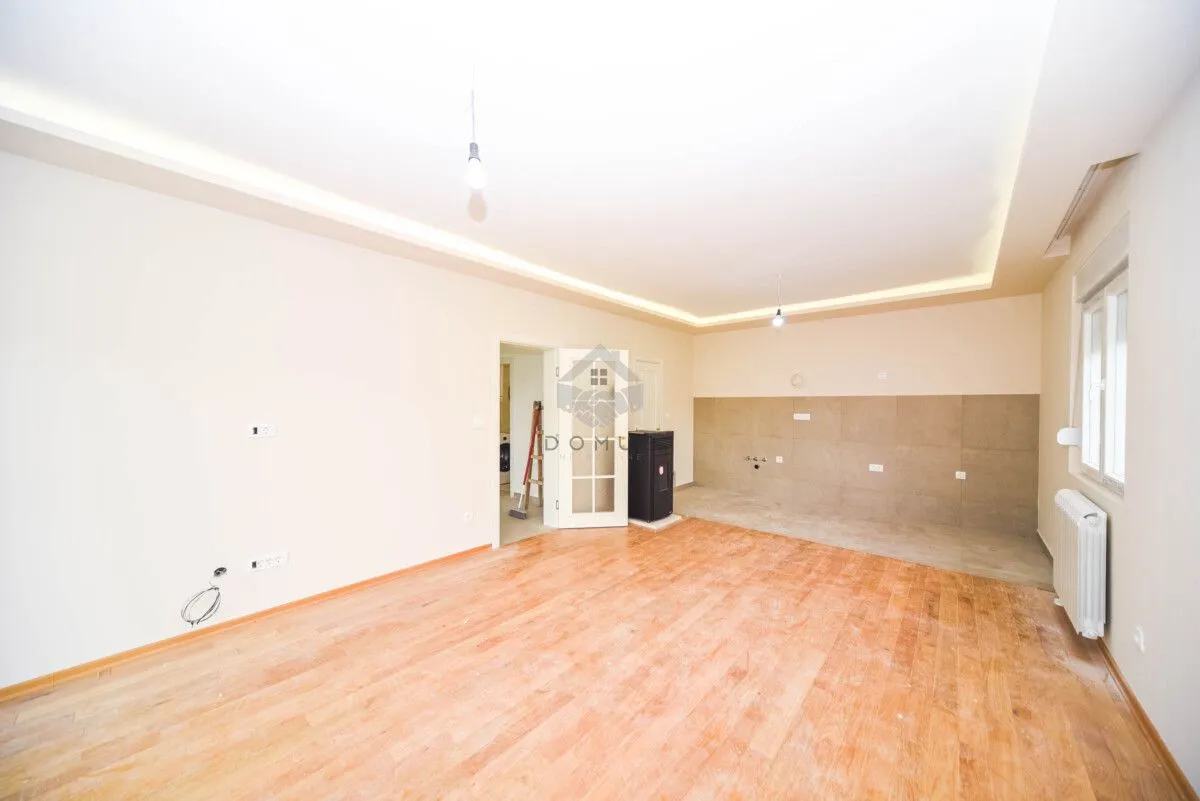 Empty living room with wooden flooring and a designated kitchen area.