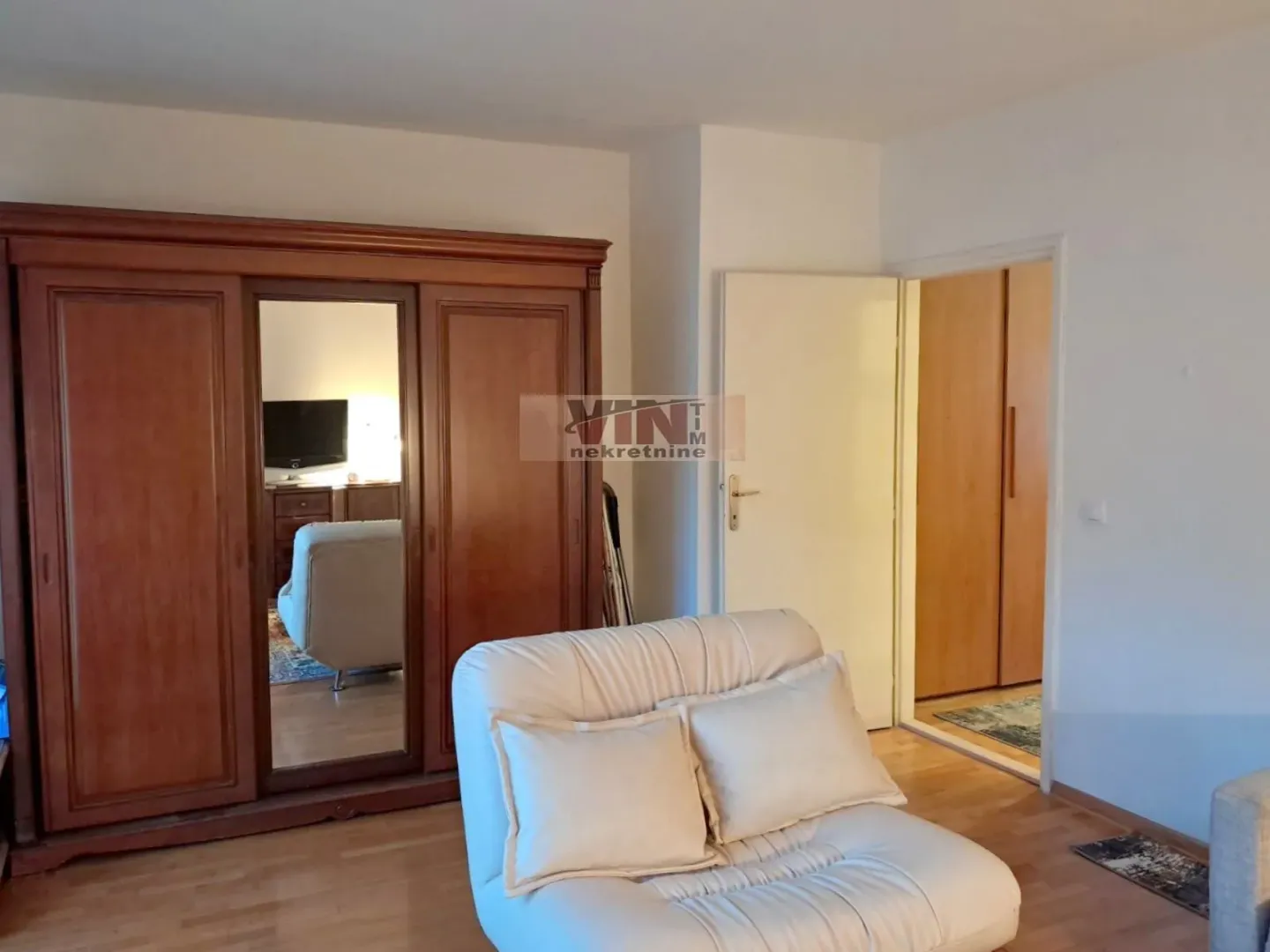 Living room with a large wooden wardrobe and a white armchair.